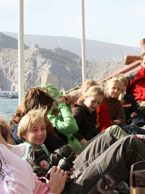 Group of people relaxing on a dhow cruise during Musandam Dibba tour with mountains in the background.