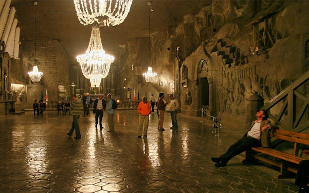 Visitors exploring the illuminated Wieliczka Salt Mine chamber with intricate wall carvings.