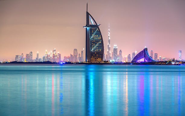 Dubai skyline at night with Burj Al Arab and city lights reflecting on the water.