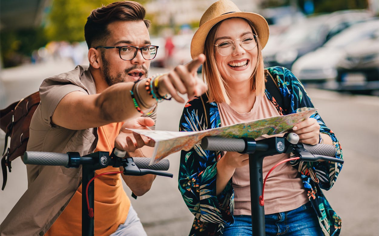 Couple on e-scooters exploring city with map during guided sightseeing tour.