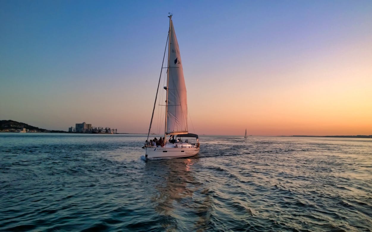Sailboat on Lisbon sunset cruise with cityscape in the background.
