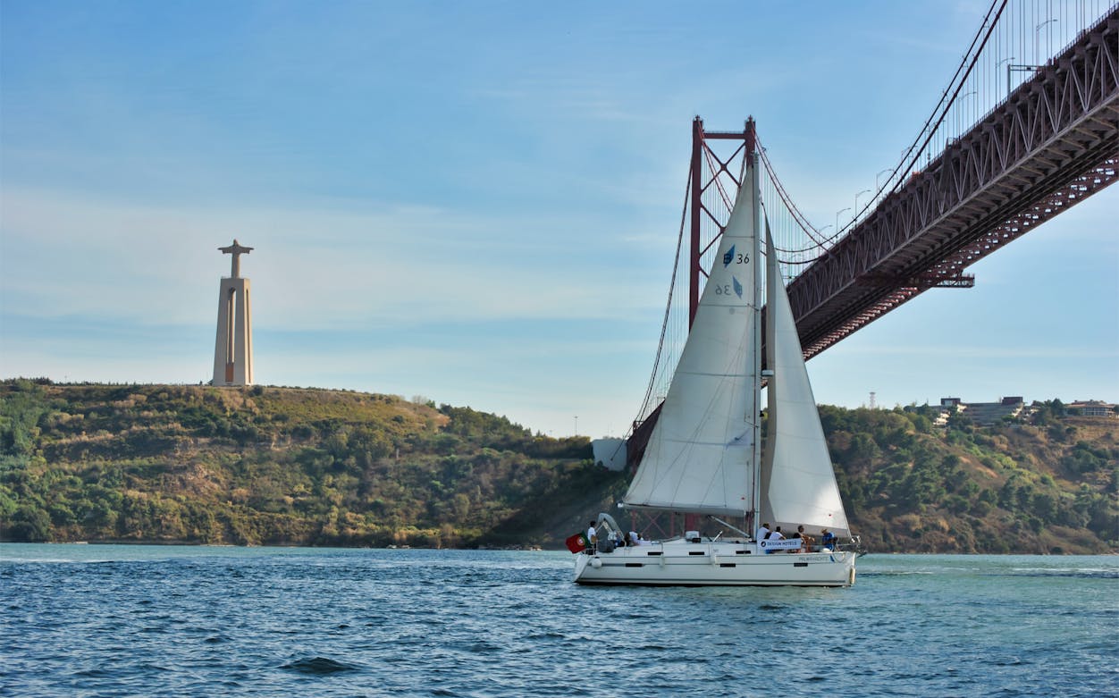 Sailboat on Tagus River near Lisbon's Christ the King statue and 25 de Abril Bridge.