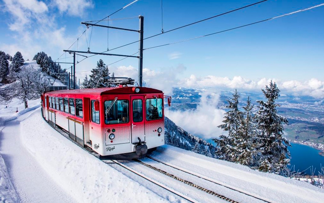 Red train ascending snowy Mount Rigi with view of Lake Lucerne, Switzerland.