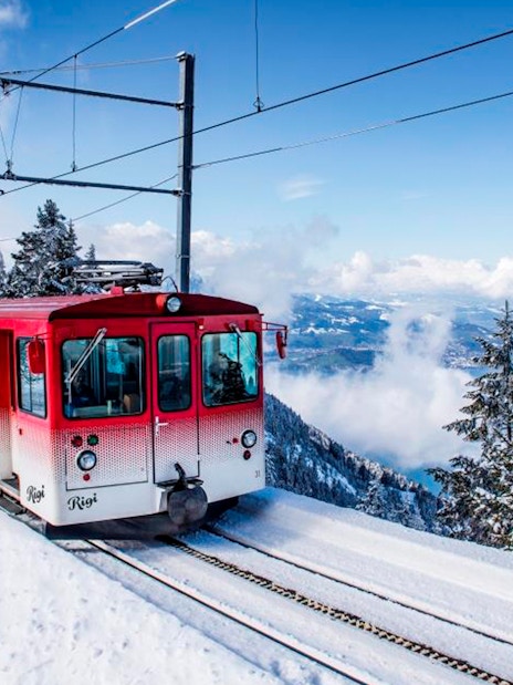 Red train ascending snowy Mount Rigi with view of Lake Lucerne, Switzerland.