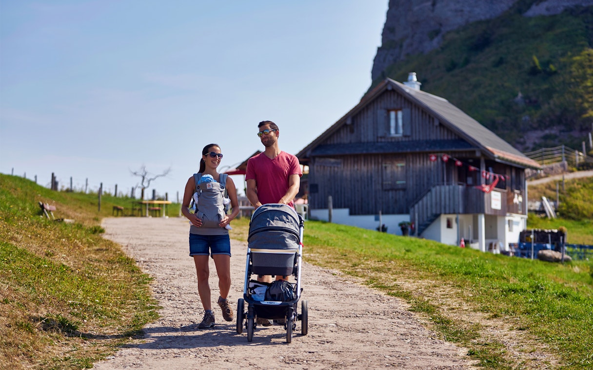 Couple walking with stroller near a chalet on Mount Rigi trail, Switzerland.