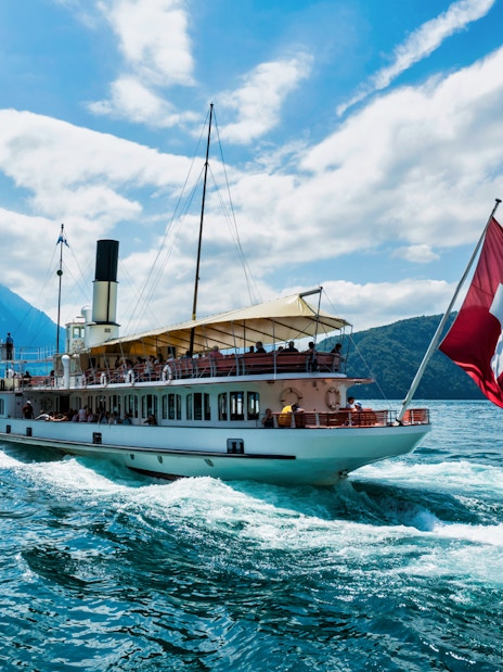 Boat on Lake Lucerne with Swiss flag, surrounded by mountains, part of Mount Rigi Day Pass tour.
