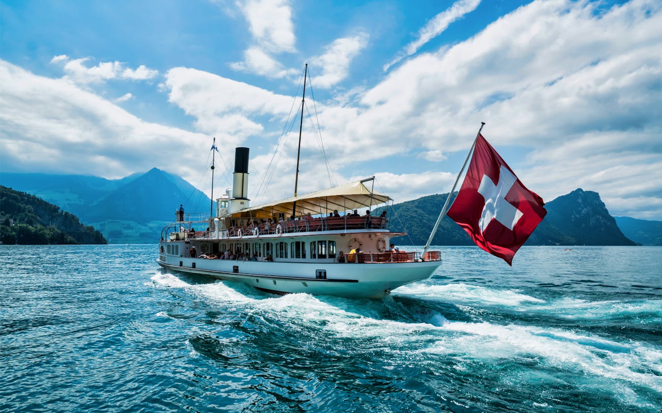 Boat on Lake Lucerne with Swiss flag, surrounded by mountains, part of Mount Rigi Day Pass tour.