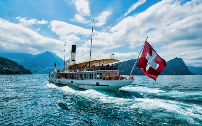 Boat on Lake Lucerne with Swiss flag, surrounded by mountains, part of Mount Rigi Day Pass tour.