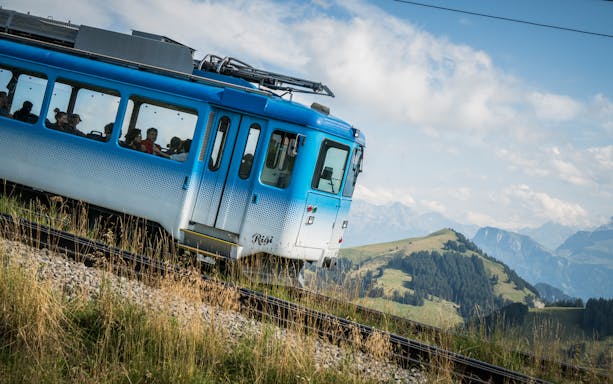 Blue train ascending Mount Rigi with passengers, scenic mountain views in Switzerland.