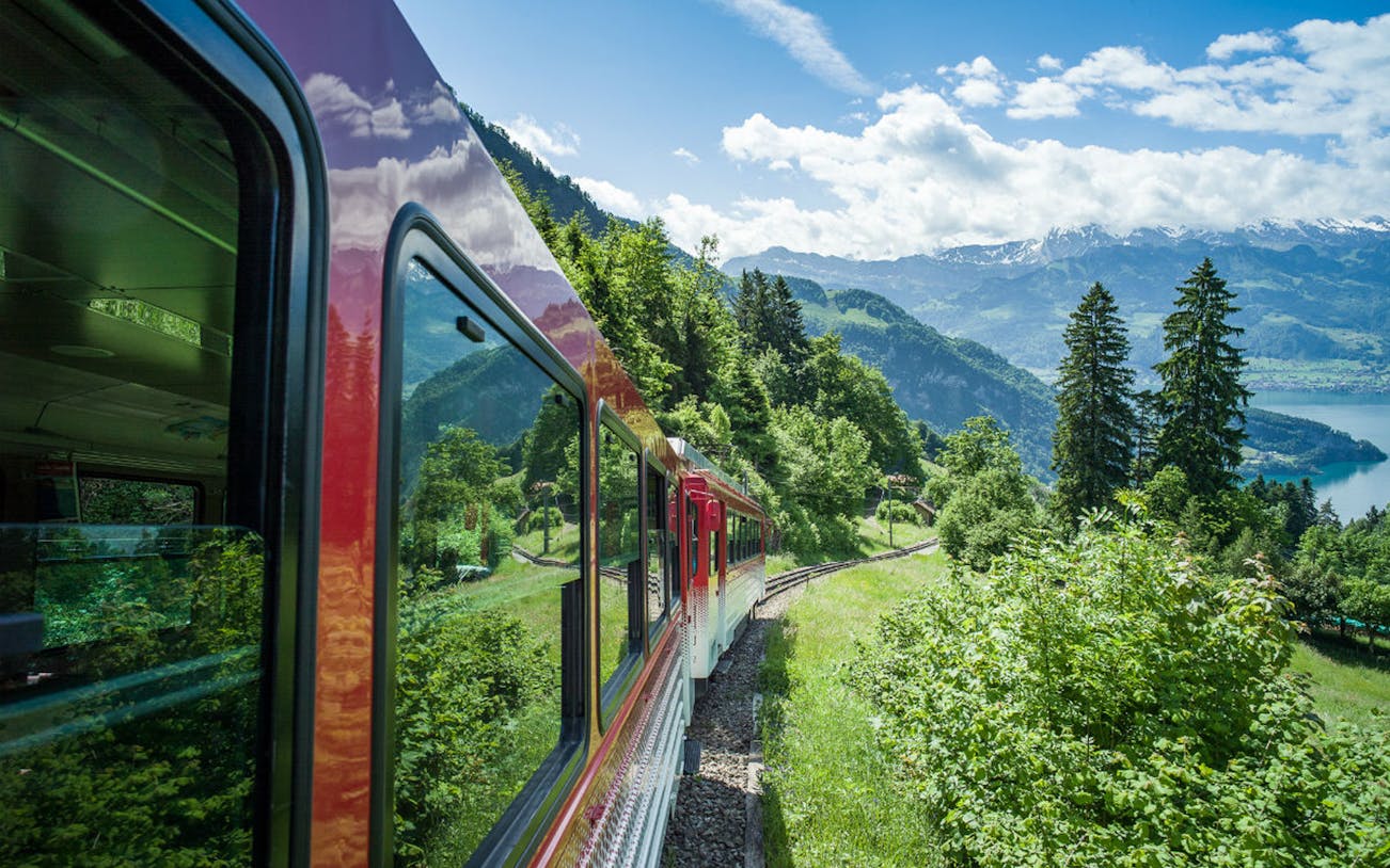 Red train traveling through lush greenery on Mount Rigi with views of Lake Lucerne, Switzerland.