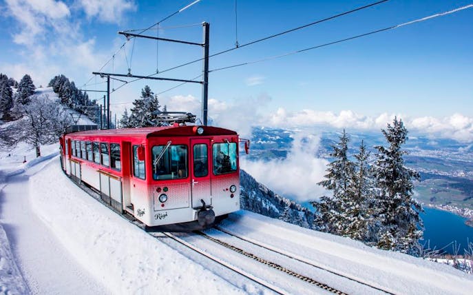 Red cogwheel train ascending snowy Mount Rigi with views of Lake Lucerne, Switzerland.