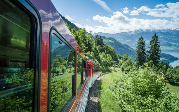 Train journey through lush greenery on Mount Rigi with views of Lake Lucerne, Switzerland.