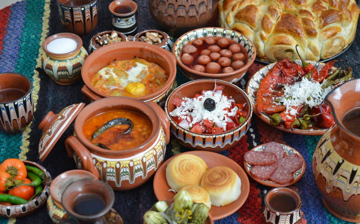 Traditional Bulgarian dishes with pottery on a colorful tablecloth, Experience Bulgaria Tour.