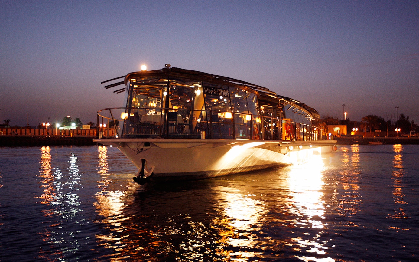 Bateaux Dubai dinner cruise on Dubai Creek at sunset with city lights reflecting on water.