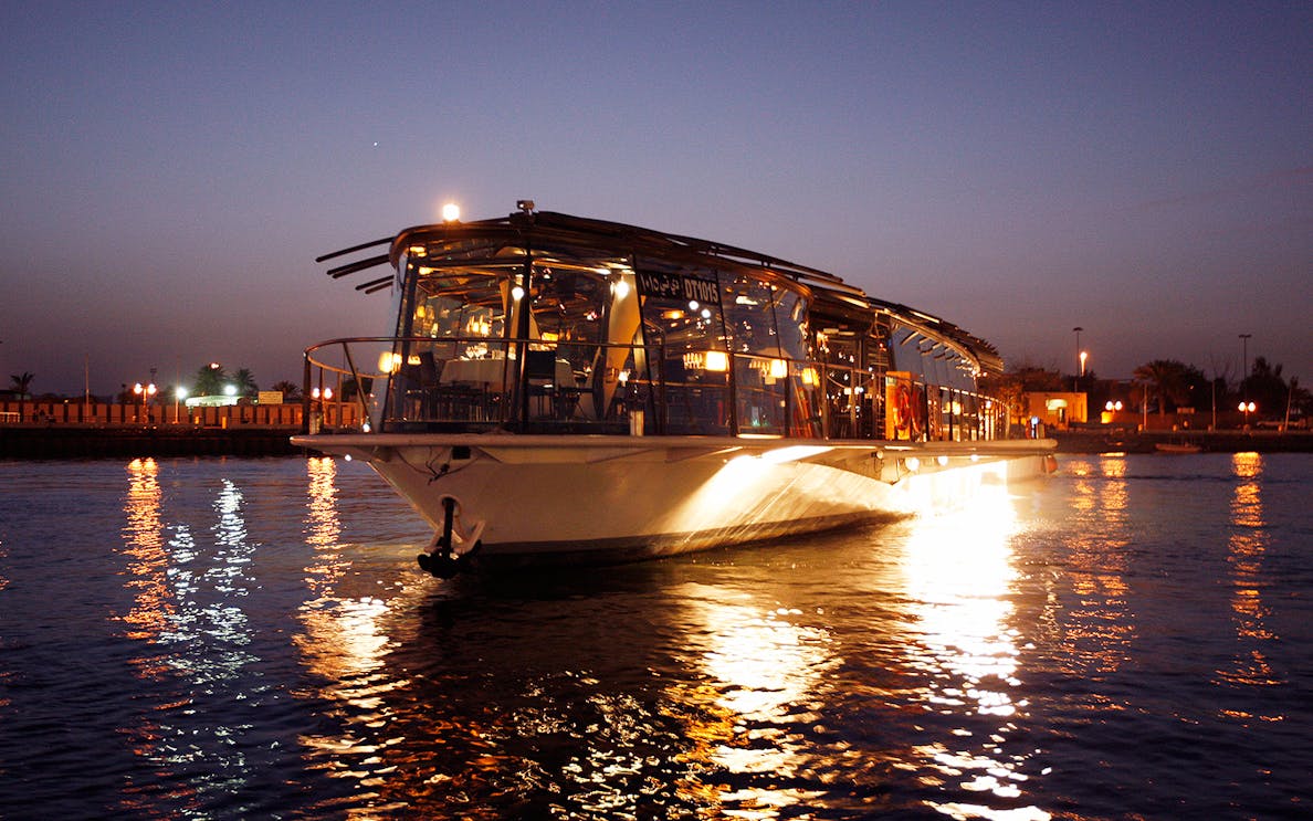 Bateaux Dubai dinner cruise on Dubai Creek at sunset with city lights reflecting on water.