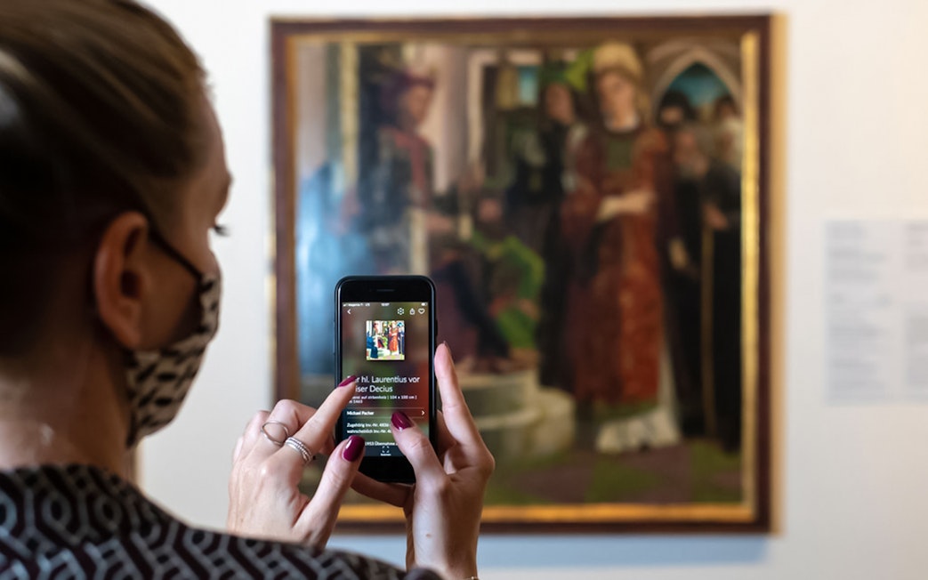 Visitor using a smartphone to view art details at Belvedere Palace, Vienna.