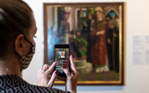Visitor using a smartphone to view art details at Belvedere Palace, Vienna.