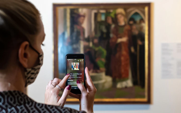 Visitor using a smartphone to view art details at Belvedere Palace, Vienna.
