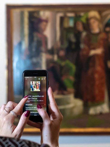 Visitor using a smartphone to view art details at Belvedere Palace, Vienna.