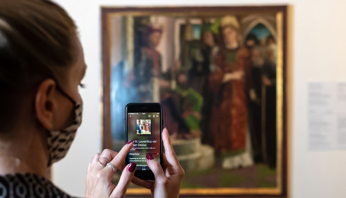 Visitor using a smartphone to view art details at Belvedere Palace, Vienna.