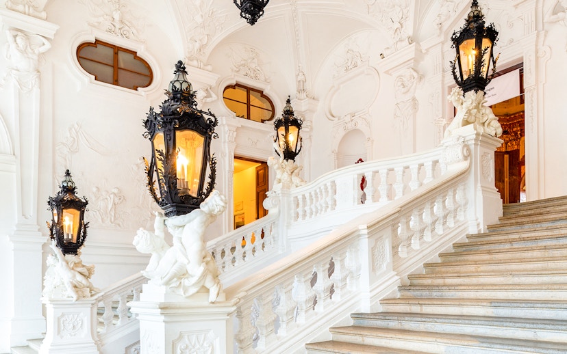 Upper Belvedere Palace interior staircase with ornate lanterns and sculptures.