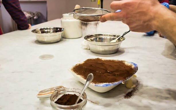 Tiramisu preparation with cocoa being sifted during a small group cooking class.