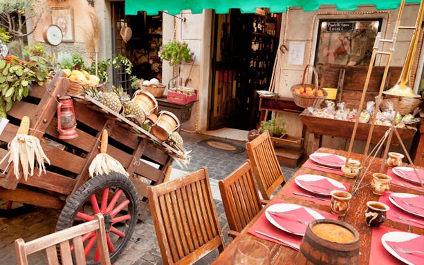 Outdoor dining setup with wooden chairs and table, surrounded by fresh produce and wine barrels in Frascati.