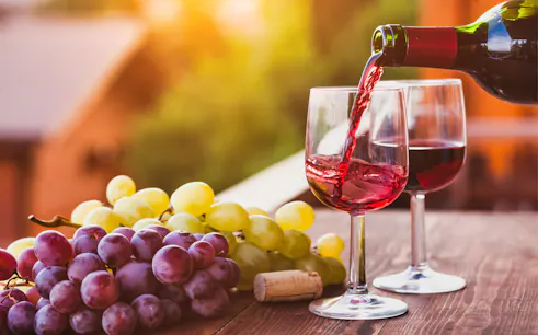 Pouring red wine into a glass with grapes on a table during Frascati Wine Tour from Rome.