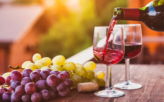 Pouring red wine into a glass with grapes on a table during Frascati Wine Tour from Rome.