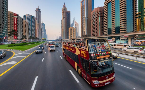 Open-top tour bus on Dubai's Sheikh Zayed Road with city skyline.
