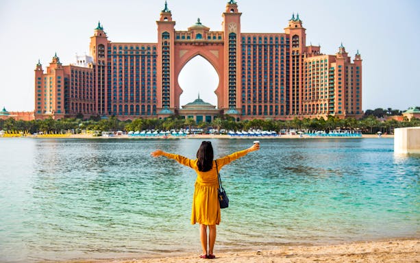Woman facing Atlantis The Palm hotel in Dubai by the water.