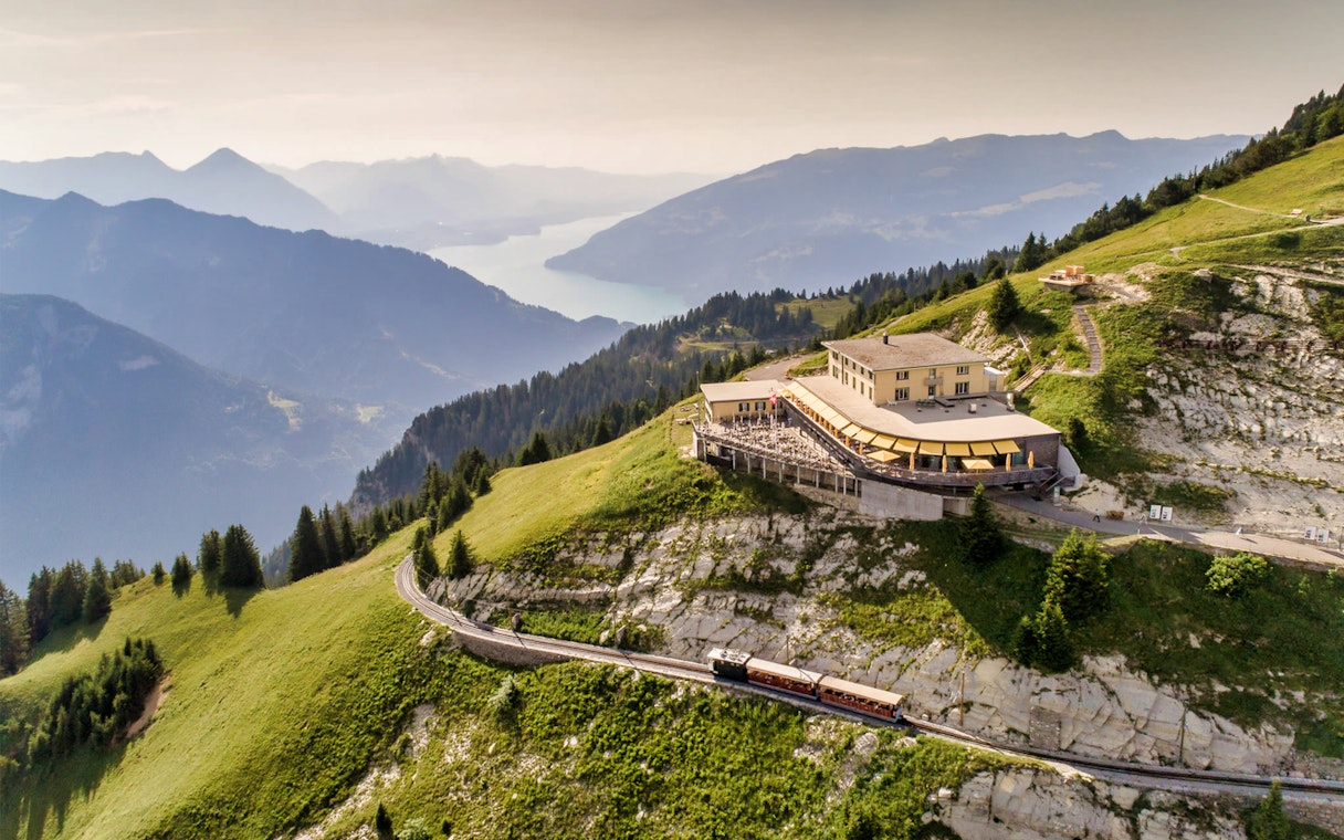Train approaching Schynige Platte station with mountain and lake views in Switzerland.