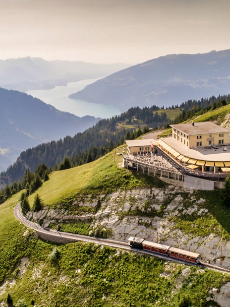 Train approaching Schynige Platte station with mountain and lake views in Switzerland.