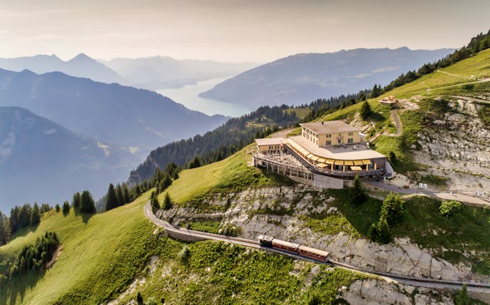 Train approaching Schynige Platte station with mountain and lake views in Switzerland.