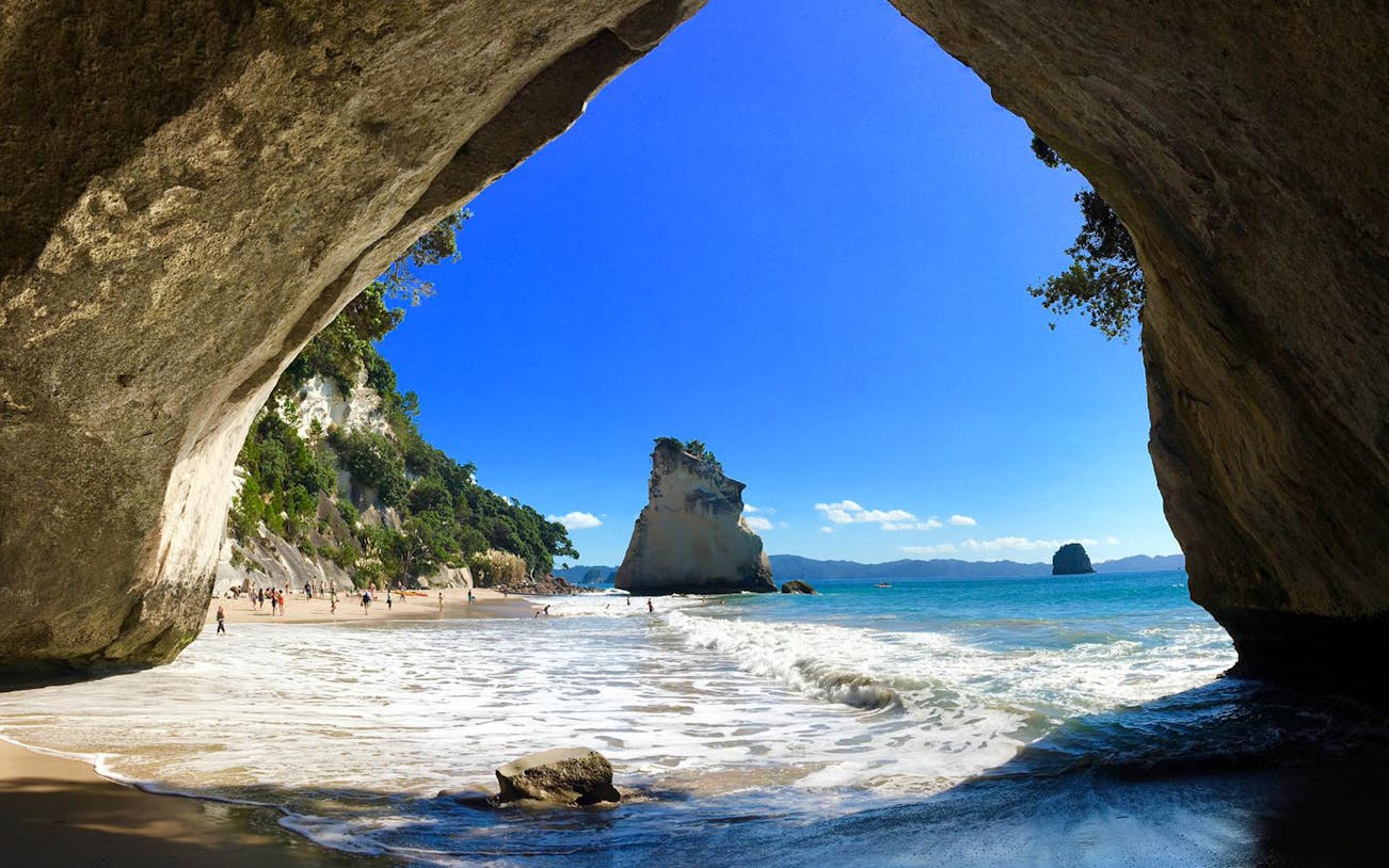 Cathedral Cove beach view, Coromandel Peninsula, with rock formations and ocean waves.