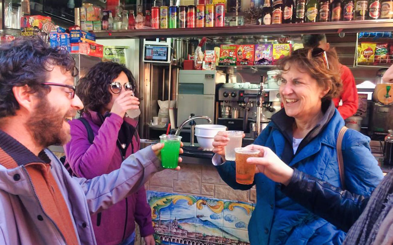 People enjoying drinks at a street food stall during a Catania Street Food Tour.