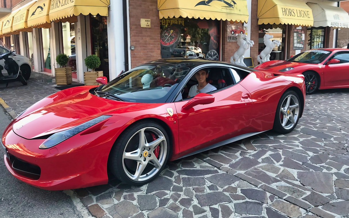 Test driving a red Ferrari 458 Italia on a cobblestone street in Maranello.
