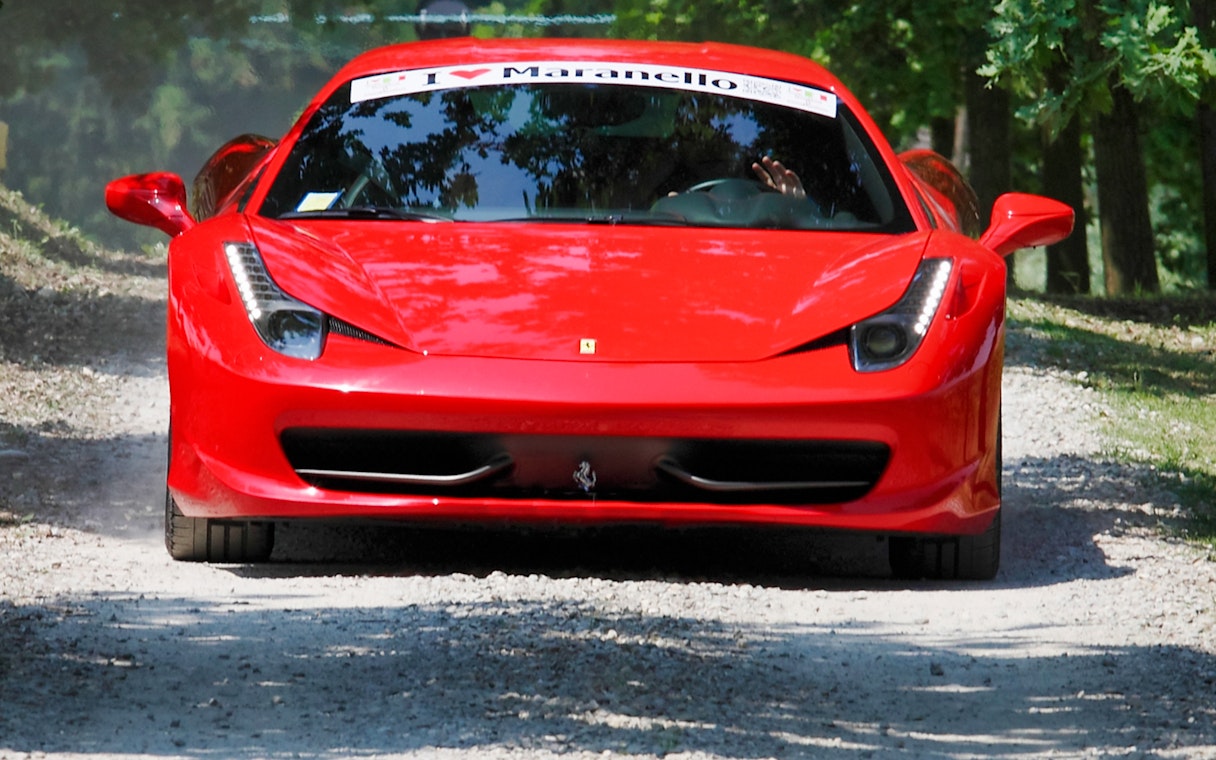 Ferrari 458 Italia driving on a tree-lined road in Maranello.