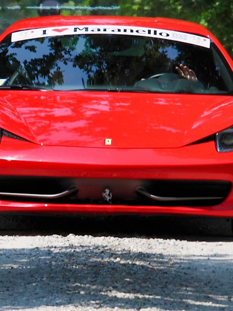 Ferrari 458 Italia driving on a tree-lined road in Maranello.
