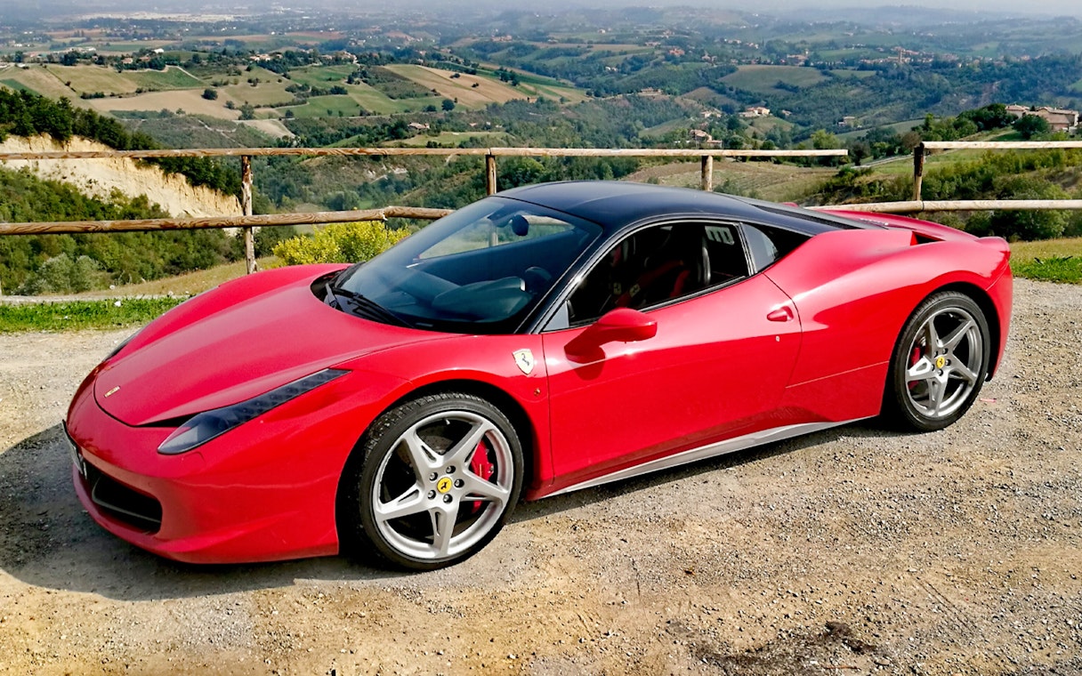Ferrari 458 Italia parked with Maranello countryside view.