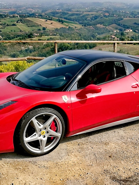 Ferrari 458 Italia parked with Maranello countryside view.