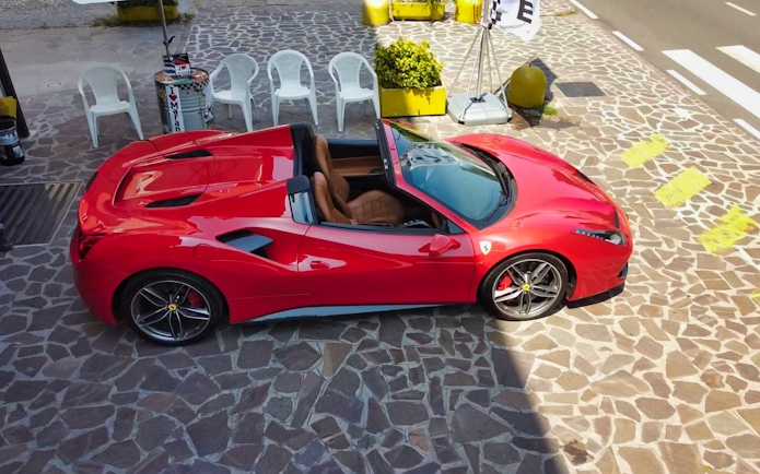 Red Ferrari 488 Spider parked on stone pavement, ready for test drive experience.