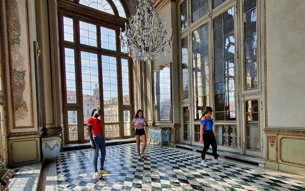 Visitors exploring the grand interior of Palazzo Madama, Turin, with large windows and chandelier.