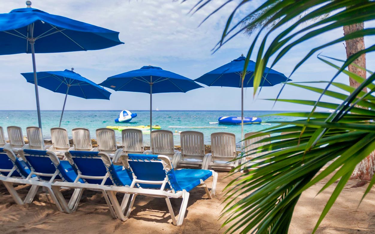 Sun loungers and umbrellas on a sandy beach with inflatables in the sea, El Cielo, Cozumel.