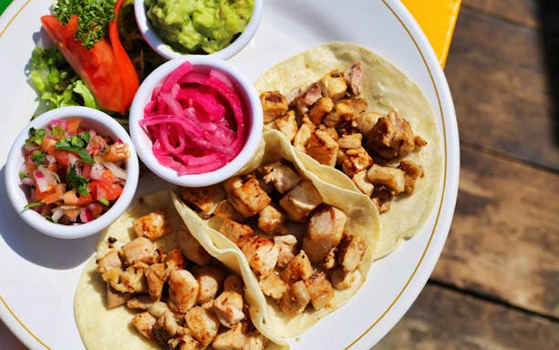 Grilled chicken tacos with guacamole, pickled onions, and salsa on a plate.