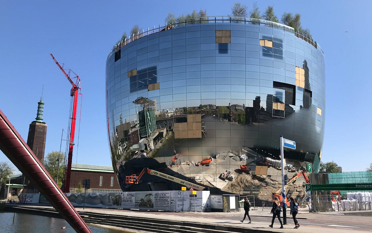 Reflective building under construction in Rotterdam with crane and pedestrians nearby.
