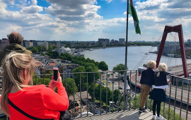 Visitors enjoying the view from the rooftop of the oldest skyscraper in Rotterdam, overlooking the river and cityscape.