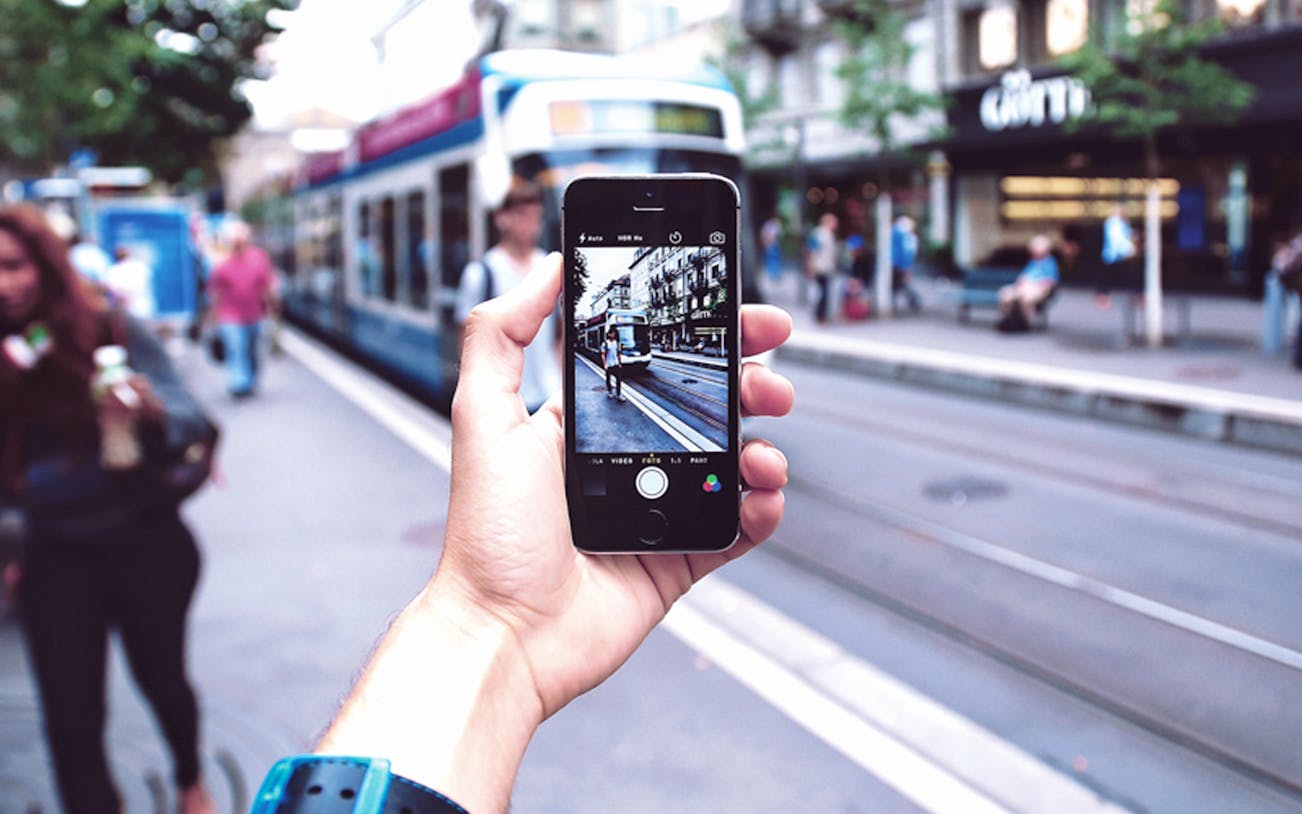 Hand holding a smartphone capturing a tram on a street in Rotterdam during the Qula City Trail.
