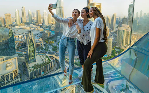Visitors taking a selfie on the glass floor of Sky Views Observatory, Dubai skyline in background.