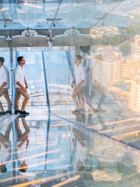 Man walking on glass slide at Sky Views Observatory with cityscape below.